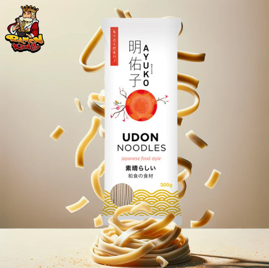 Ein Werbebild für Ayuko Udon Nudeln, auf dem eine Packung mit den Nudeln in der Mitte des Bildes steht, aus der Udon-Nudelstränge in einer lebhaften Bewegung herauszuspringen scheinen, vor einem neutralen Hintergrund.