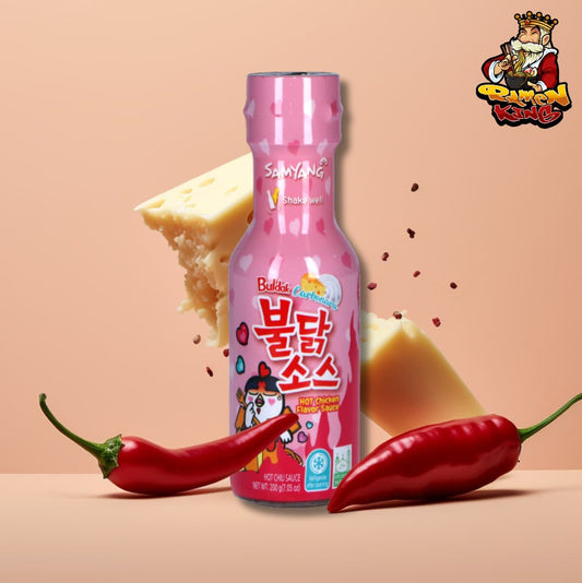 Buldak Hot Chicken Flavor Sauce in einer rosa Flasche mit Chilischoten und Käsestücken auf einem pfirsichfarbenen Hintergrund.